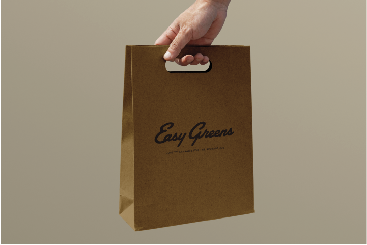 A hand holding an Easy Greens kraft paper bag with the brand's script logo